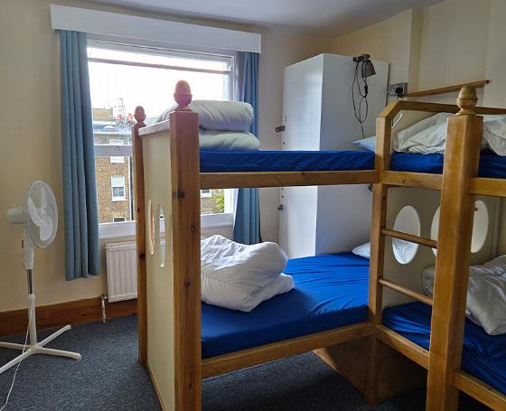 bunk beds in a cozy room with white linens and blue bedding near a window with curtains and a fan offering comfortable sleeping arrangements